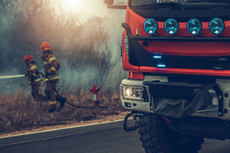 Modern European Fire Truck and Two Firefighters Fighting Grass Wildfire in Background