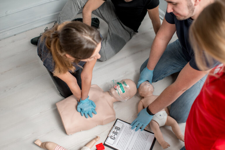 Group of people learning how to make first aid heart compressions with dummies during the training indoors