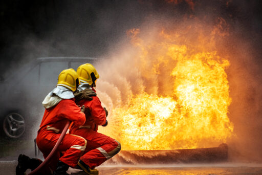 Two Firefighter teamwork in fire suit with fire fighting equipment using high pressure water fight a fire Two Firefighter teamwork in fire suit with fire fighting equipment using high pressure water fight a fire