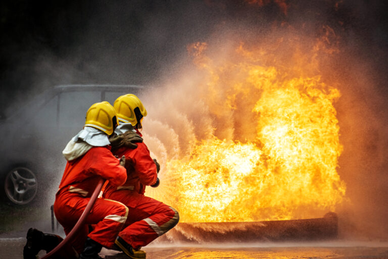 Two Firefighter teamwork in fire suit with fire fighting equipment using high pressure water fight a fire