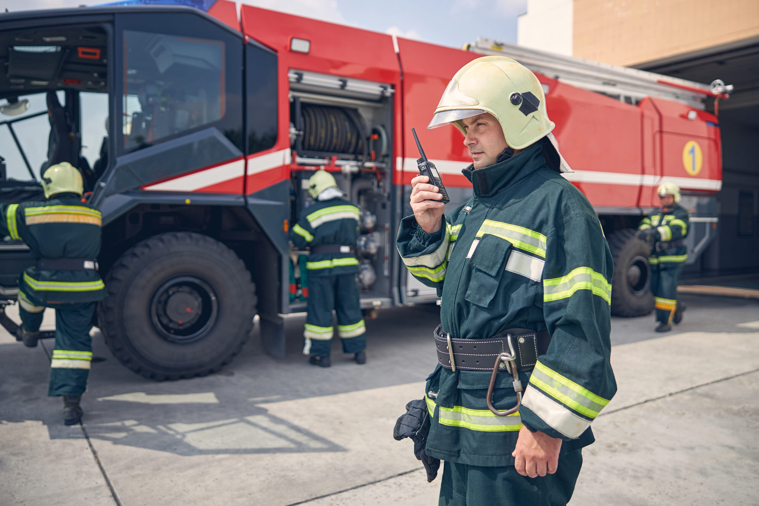 Waist up portrait of firefighter standing in the outdoor in front of firefighter crew and fire engine machine